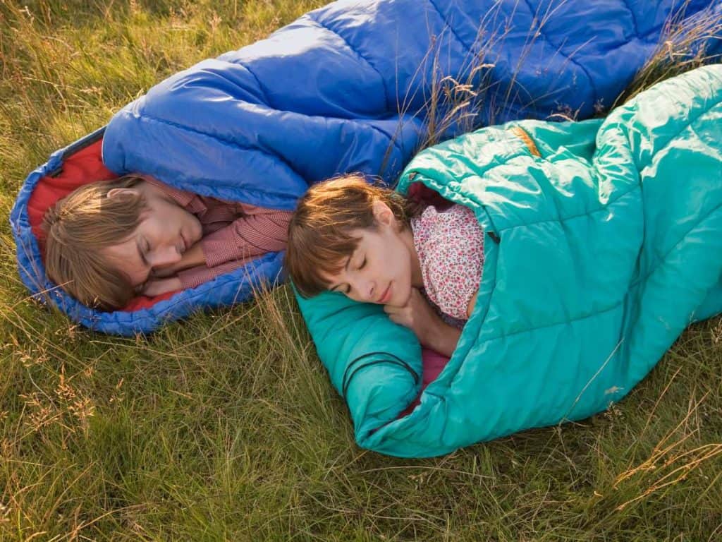 A couple relaxing next to each other in sleeping bags, illustrating the different types when it comes to how to choose a sleeping bag