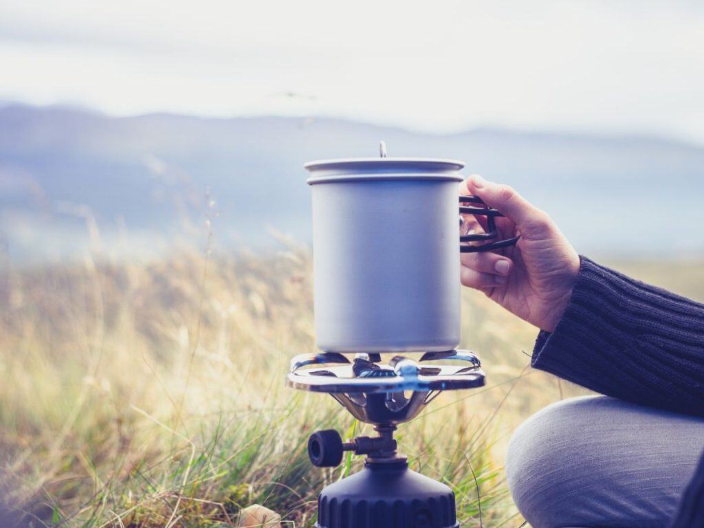 Simple budget camping stove boiling water in a metal pot outdoors, showing an affordable option for the best camping stove for casual trips.
