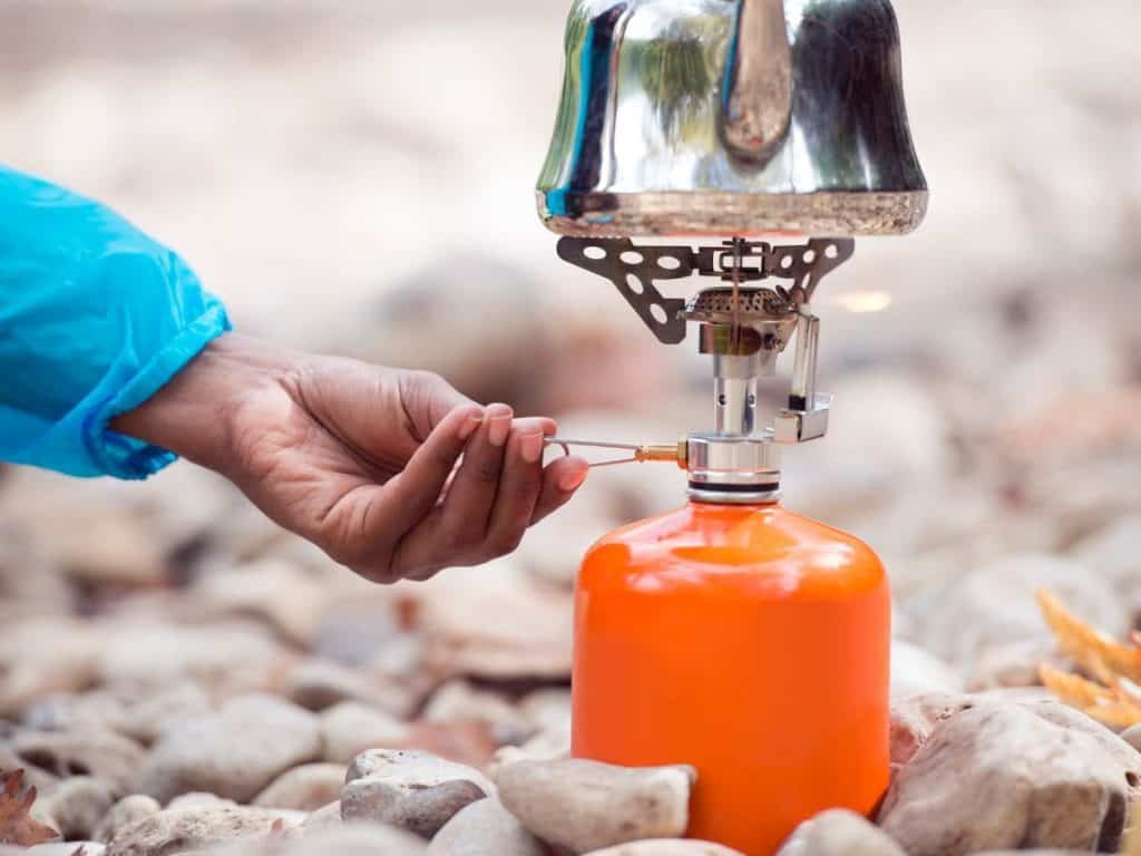 Camper adjusting a gas camping stove fuel canister with a kettle attached, explaining different fuel options for the best camping stove.