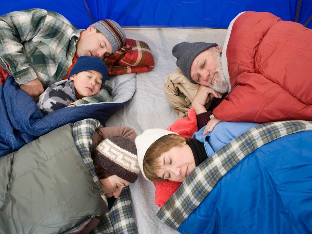 Family sleeping side by side inside a tent, wrapped in thick sleeping bags, showing how warmth and comfort play a huge role in getting decent sleep while camping.