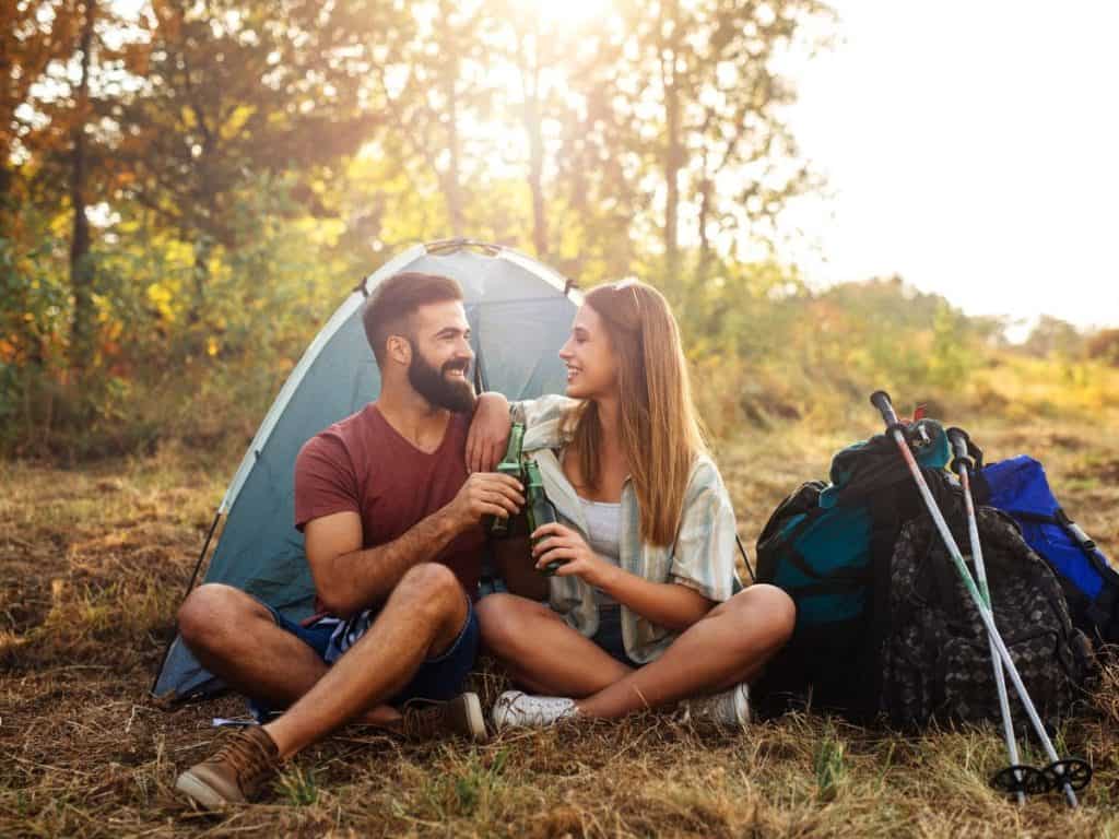 Couple relaxing at a campsite beside a tent and hiking gear, highlighting what to consider before choosing the best camping stove for your trips.