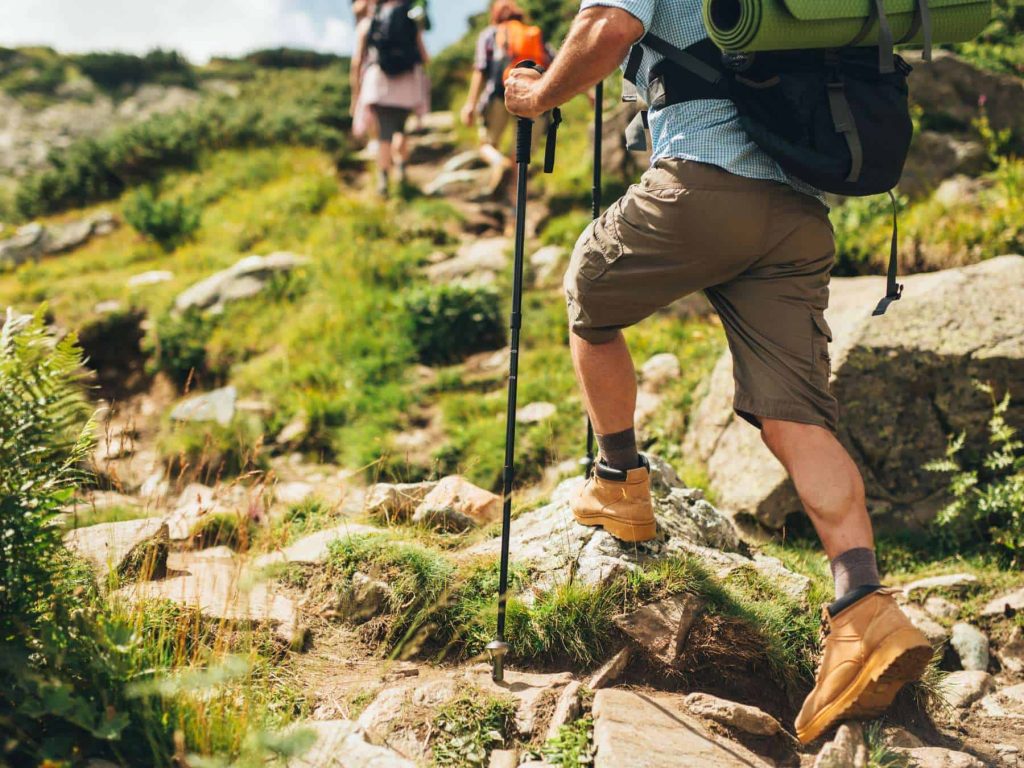 Is sleeping on the ground while camping bad for your back? Hikers trekking on rocky terrain, highlighting back pain risks, sleeping pads, camping mattresses and spinal support when camping.