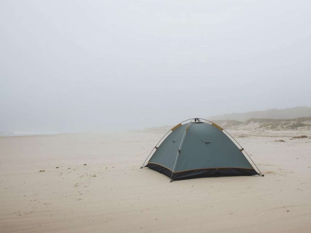 Small dome tent set up on a wide, empty sandy beach under overcast skies - minimalist coastal scene illustrating choosing the right beach for safe and sheltered camping.