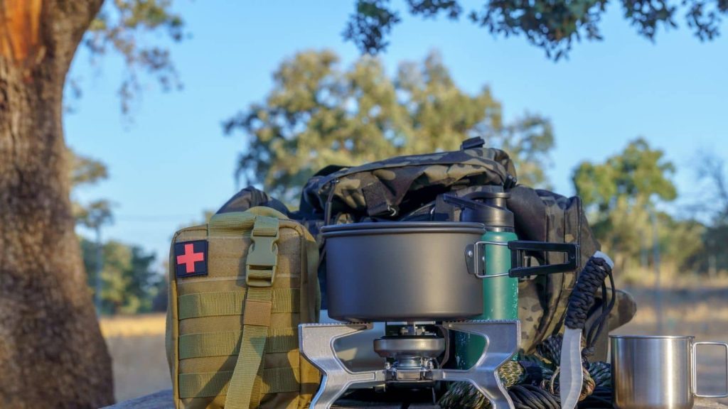 Reusable camping equipment set up outdoors, including a refillable water bottle, metal cookware on a portable stove, and durable storage bags - illustrating the shift away from single-use items toward long-lasting, sustainable gear choices for eco-friendly camping.