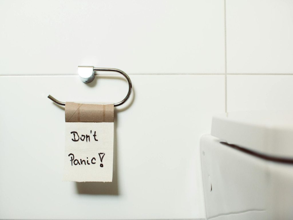 Toilet paper on a holder with a “don’t panic” note, highlighting common camping mistakes like forgetting essential supplies.