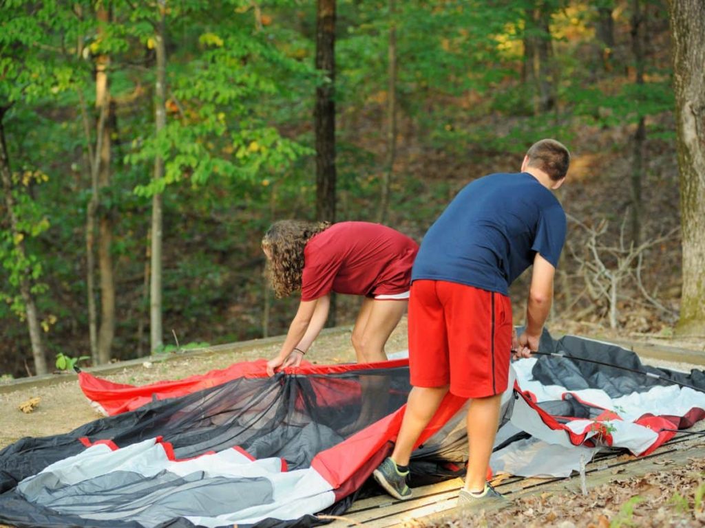 Teenagers setting up a tent on uneven ground, showing the real side of camping with teenagers