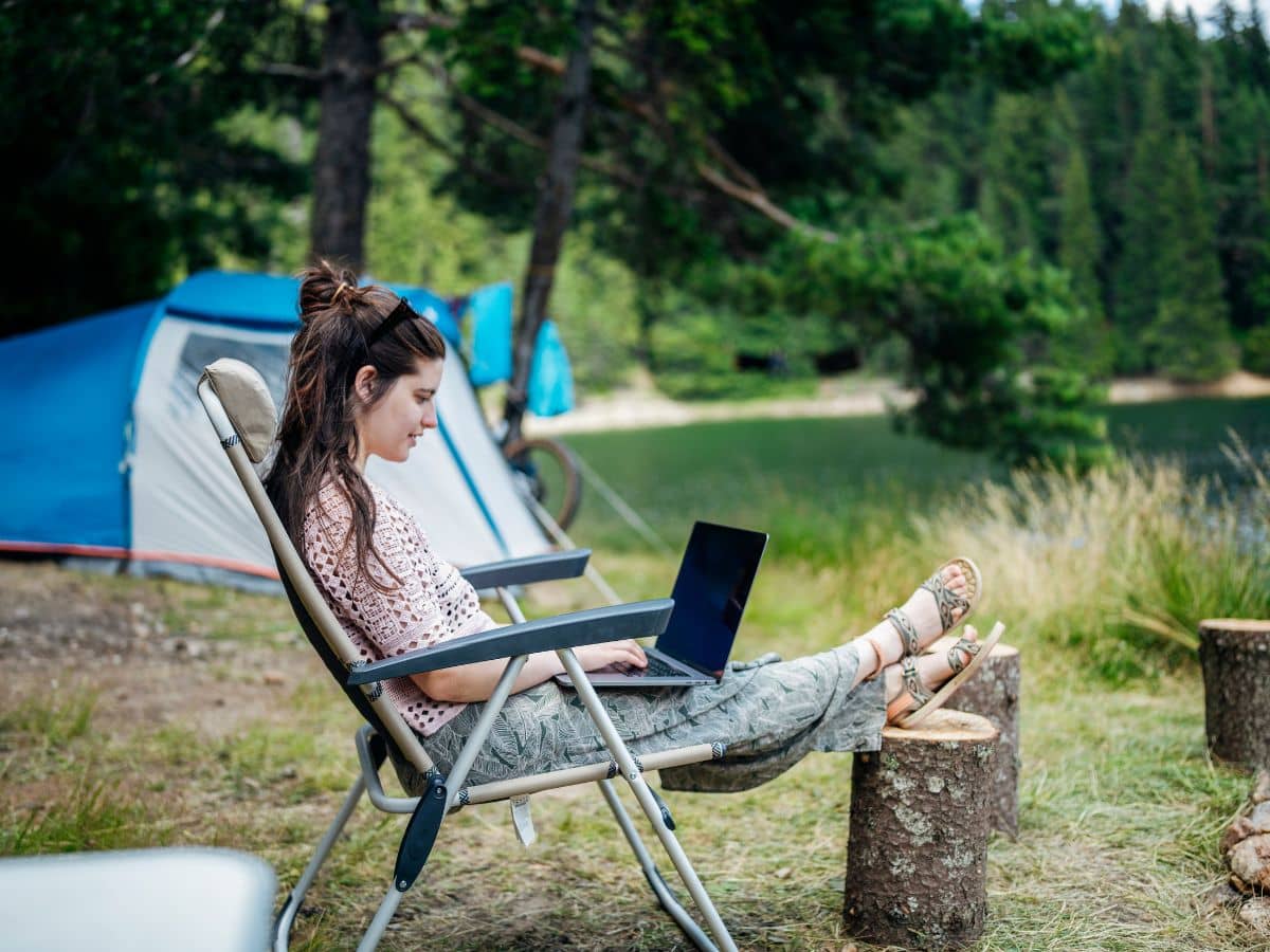Person relaxing with a laptop at a lakeside campsite, showing how to balance work and enjoying the outdoors while camping.