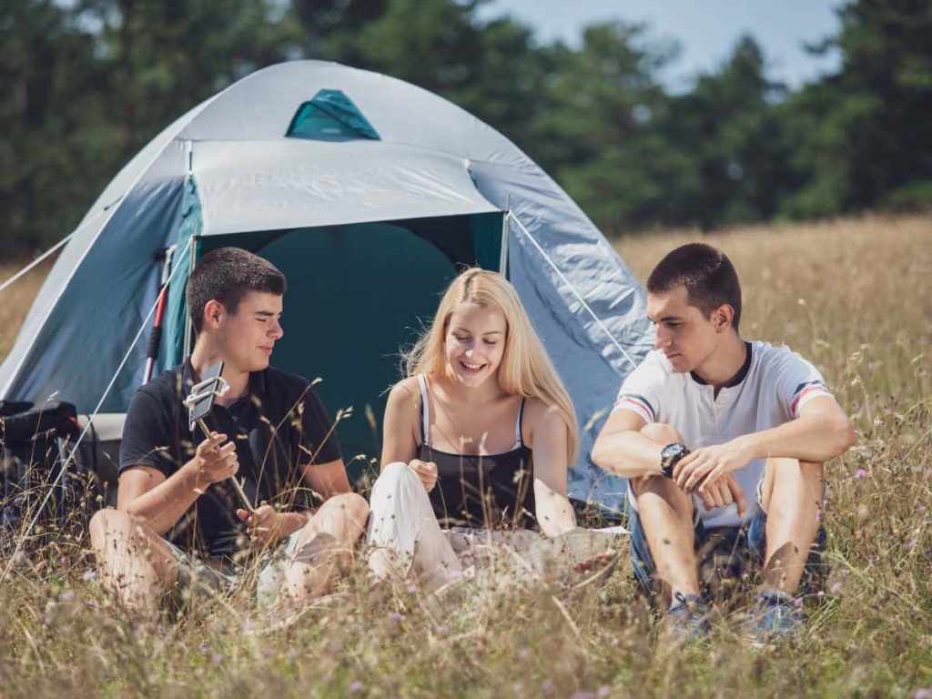 Teenagers relaxing by a tent in a field, showing how camping with teenagers can be comfortable and enjoyable