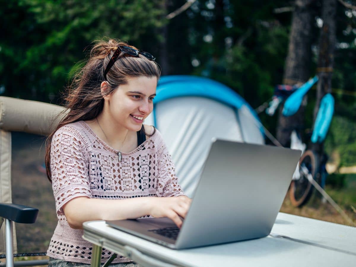 Person using a laptop at a campsite, showing how choosing the right campsite affects working while camping.