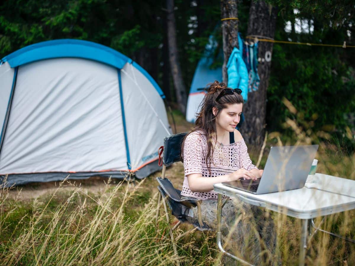 Person working on a laptop at a campsite table, showing how to create a workspace while camping.