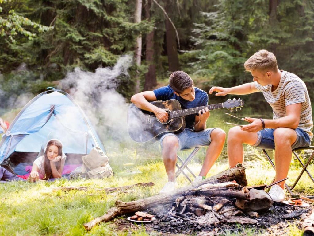 Teenagers relaxing at a campsite playing guitar and hanging out, showing the natural side of camping with teenagers