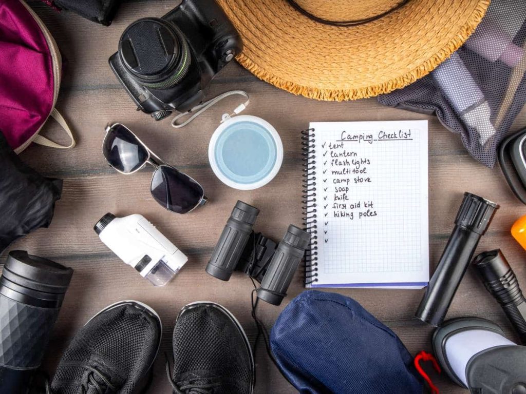 Camping gear and packing checklist laid out on table, showing how to pack camping gear for air travel.