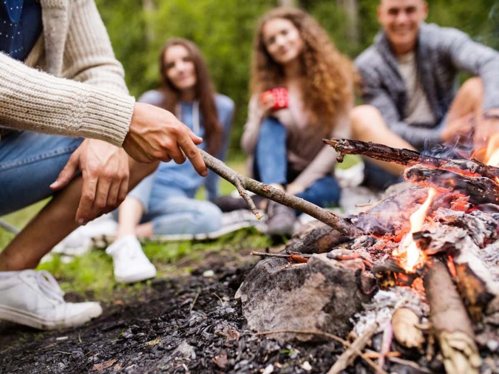 Teenagers relaxing by a campfire, highlighting the shared experience of camping with teenagers