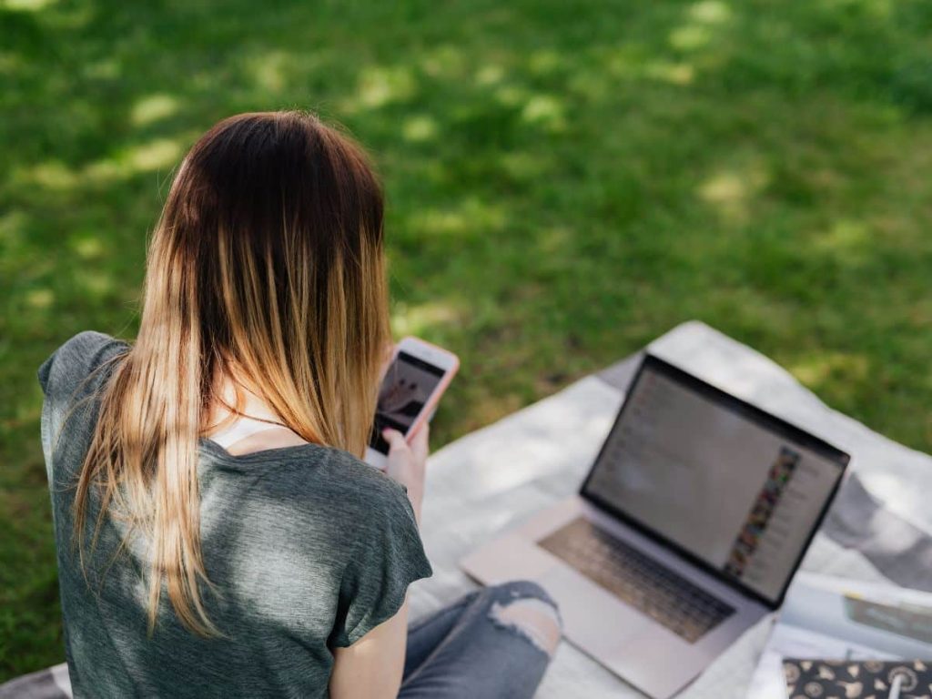 Teenager using a phone and laptop outdoors, showing how camping with teenagers can include balanced use of technology
