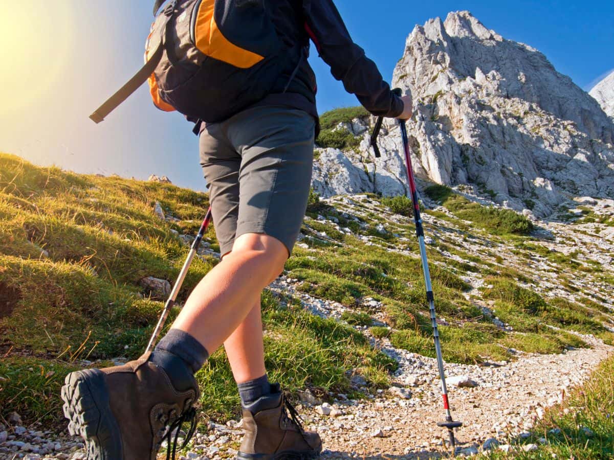 Hiker walking uphill with boots and poles, showing how to stop blisters when hiking before they get worse.