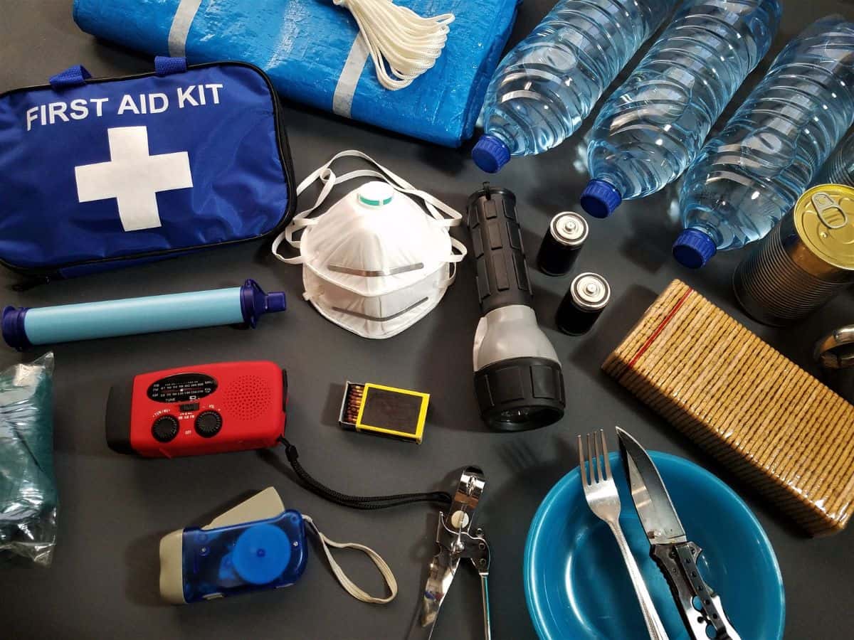 First aid kit, bottled water, torch, emergency radio and other safety supplies laid out together, highlighting first aid and personal medication when deciding what to pack for a day hike.