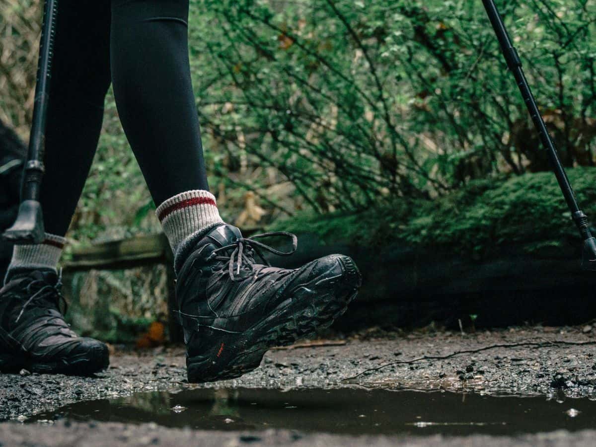 Close-up of wet hiking boots stepping beside a puddle on a muddy woodland trail, illustrating why it helps to know how to dry hiking boots overnight after a damp day outdoors.
