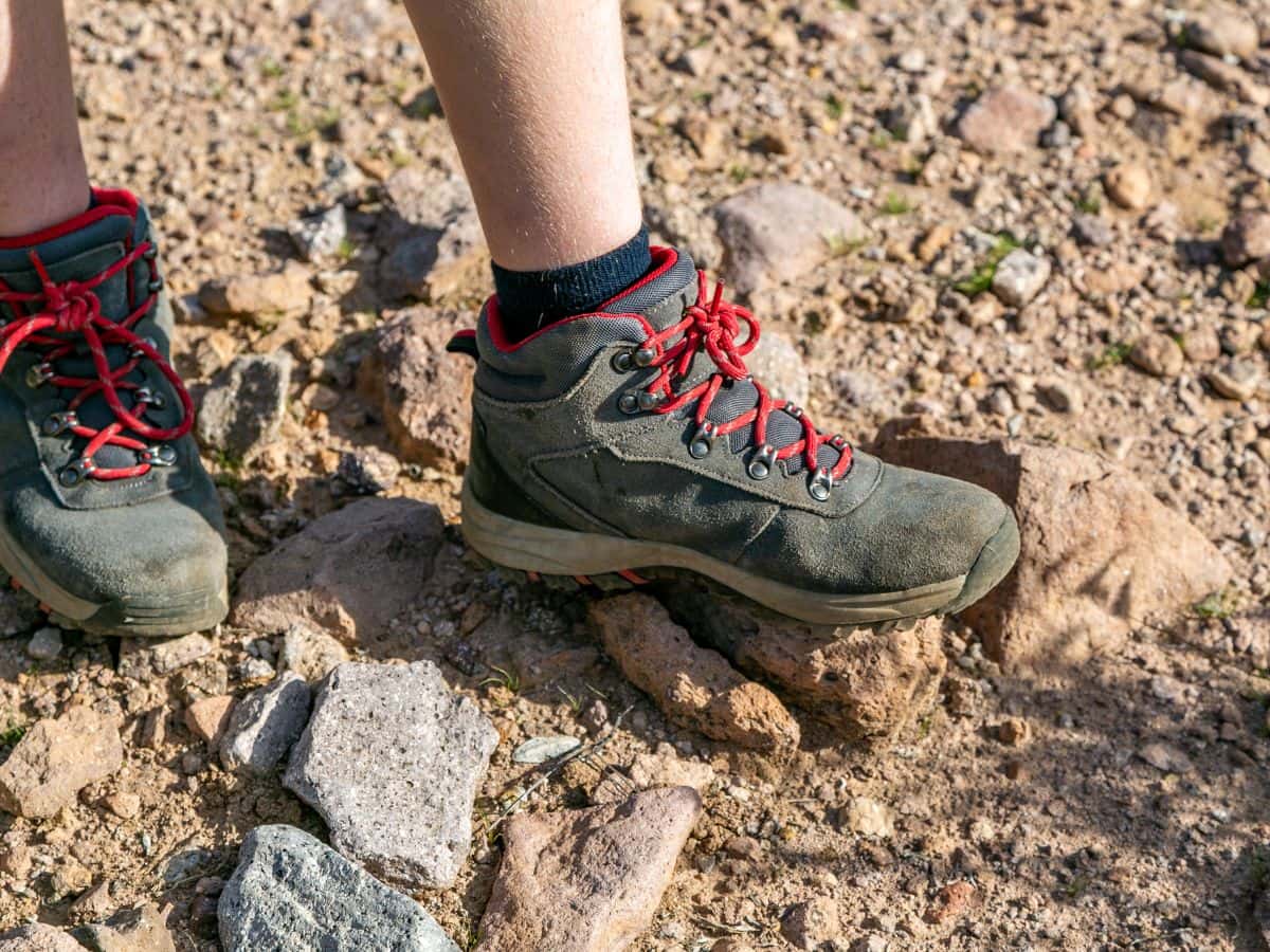 Close-up of hiking boots with red laces on rocky ground, illustrating how to deal with wet hiking boots while camping and what to do when you cannot fully dry hiking boots overnight.