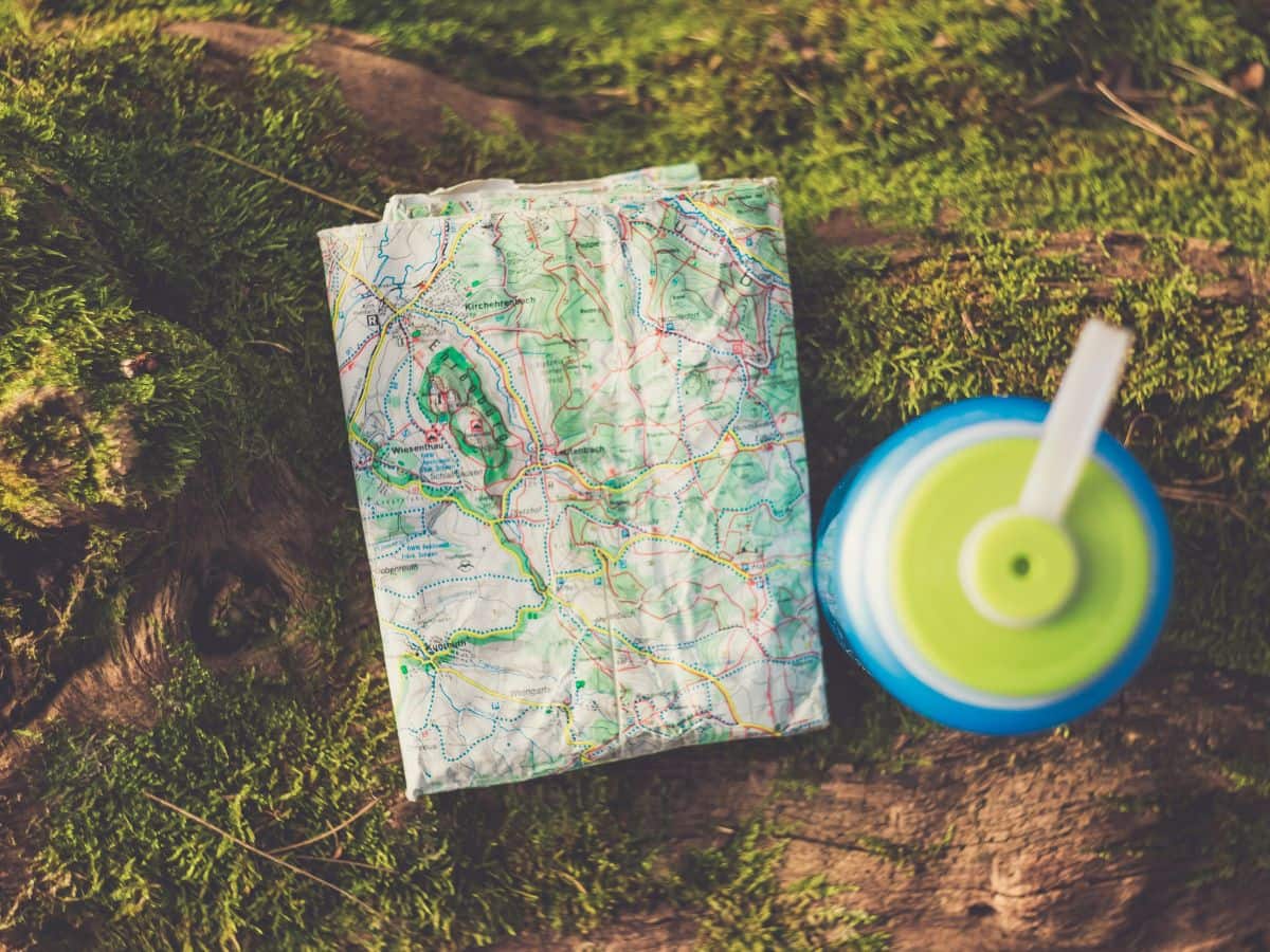 Folded hiking map and reusable water bottle resting on a mossy woodland floor, highlighting navigation and hydration essentials when deciding what to pack for a day hike.