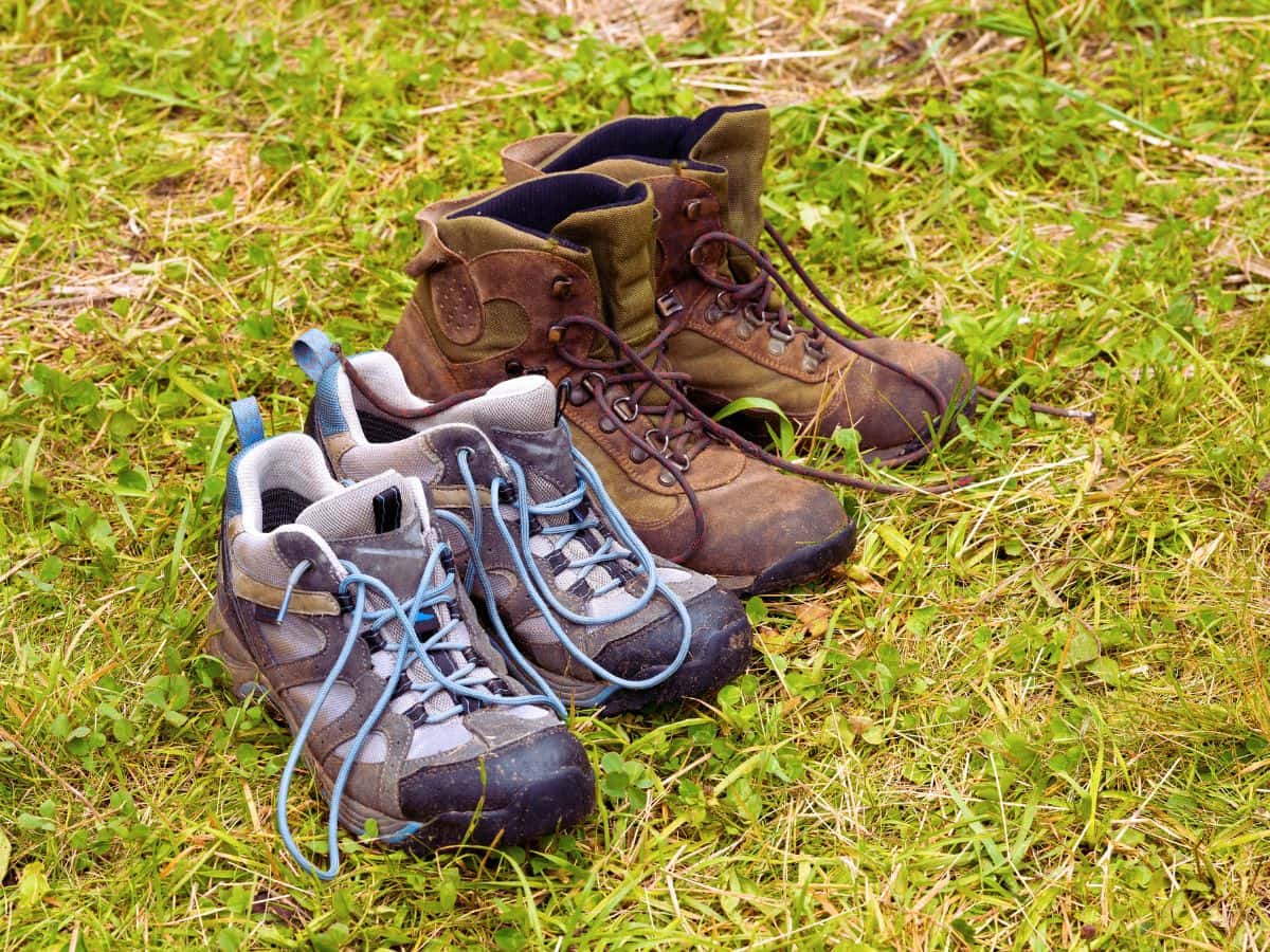 Two pairs of hiking boots left open on grass with their laces loosened, illustrating the best way to dry hiking boots overnight by removing moisture and allowing air to circulate properly.