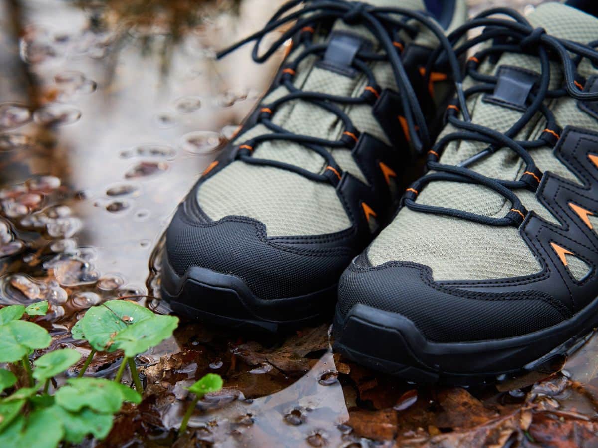 Close-up of wet hiking shoes sitting beside puddles and forest leaves, illustrating what not to do when learning how to dry hiking boots overnight after a rainy walk.