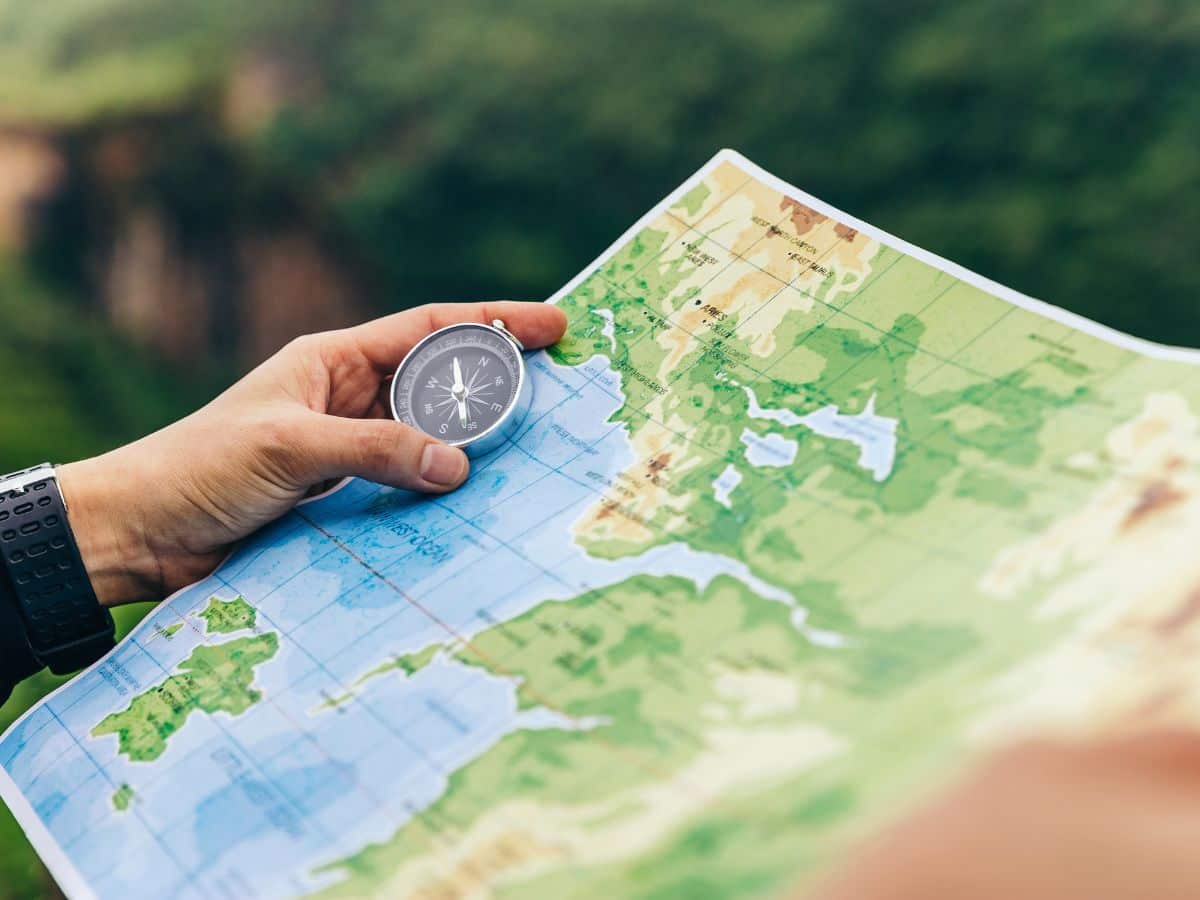 Close-up of a hiker holding a compass over a paper map, illustrating simple ways to prevent and relieve swollen hands while hiking by adjusting movement, hydration and trail habits.