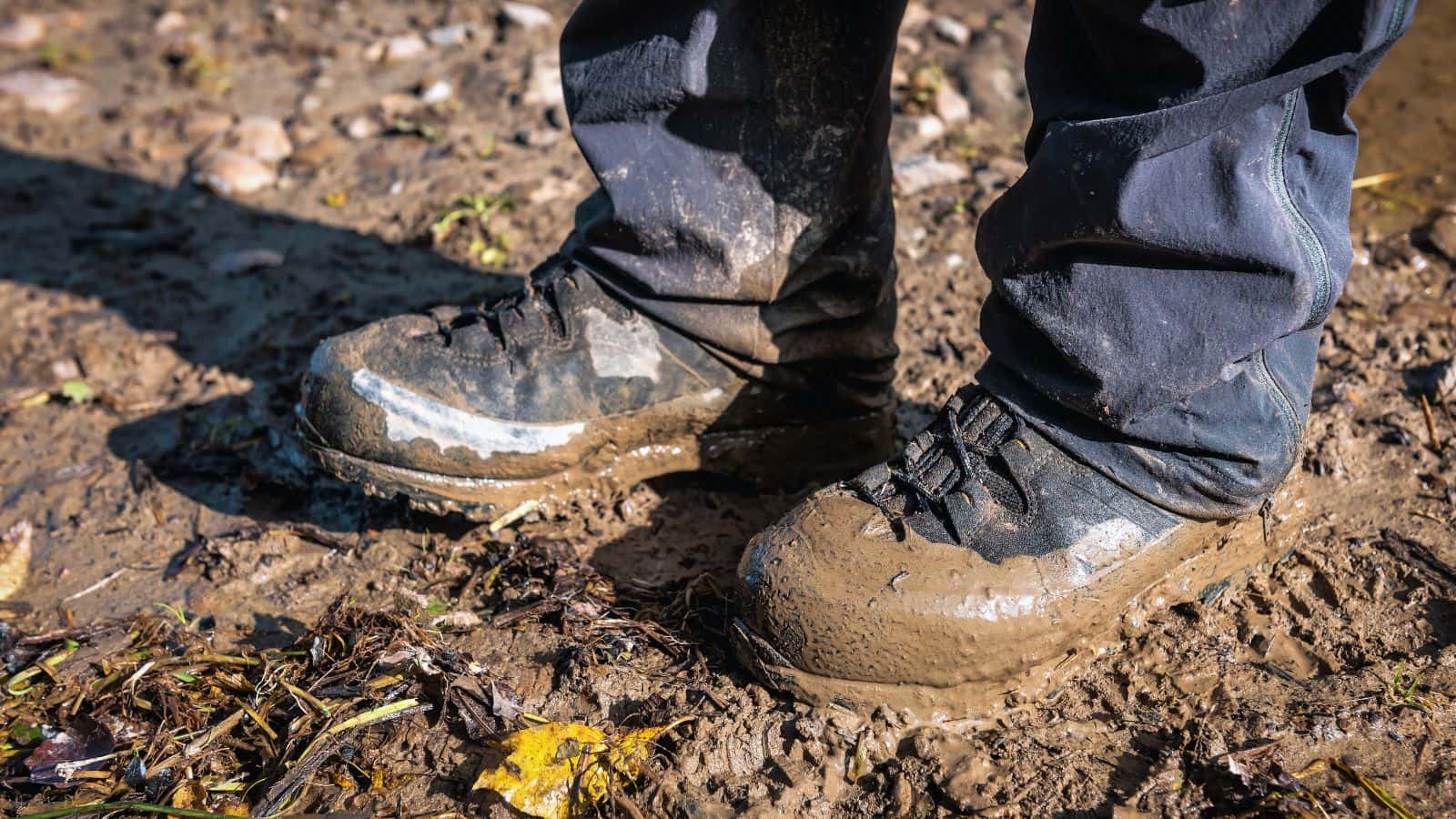 Close-up of hiking boots stuck in thick mud on a wet trail, illustrating how to get unstuck safely during a hike through deep mud without pulling a boot off.