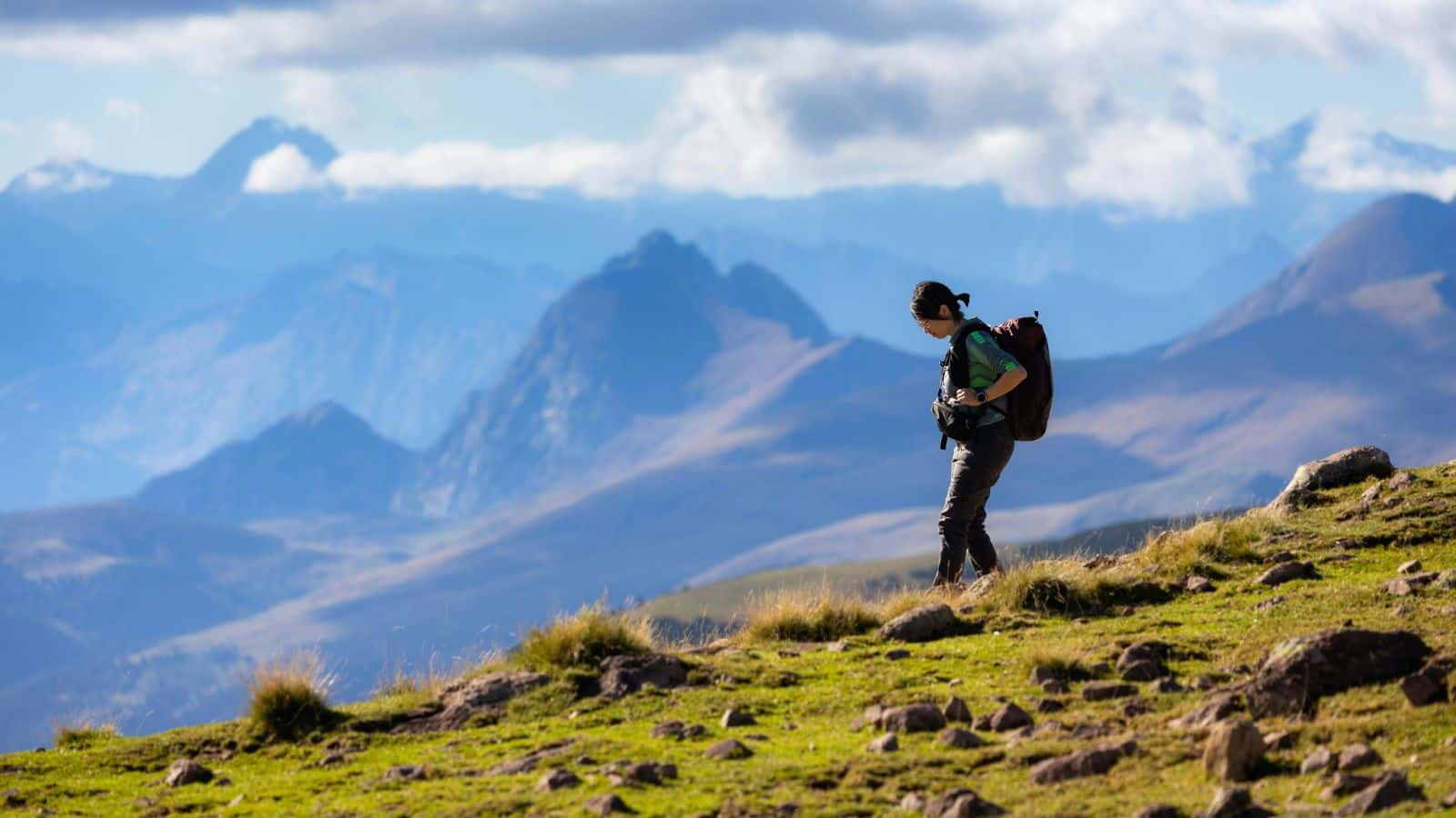 A solo female hiker carrying a backpack as she descends a grassy mountain ridge, illustrating the impact of knee pain when hiking downhill.