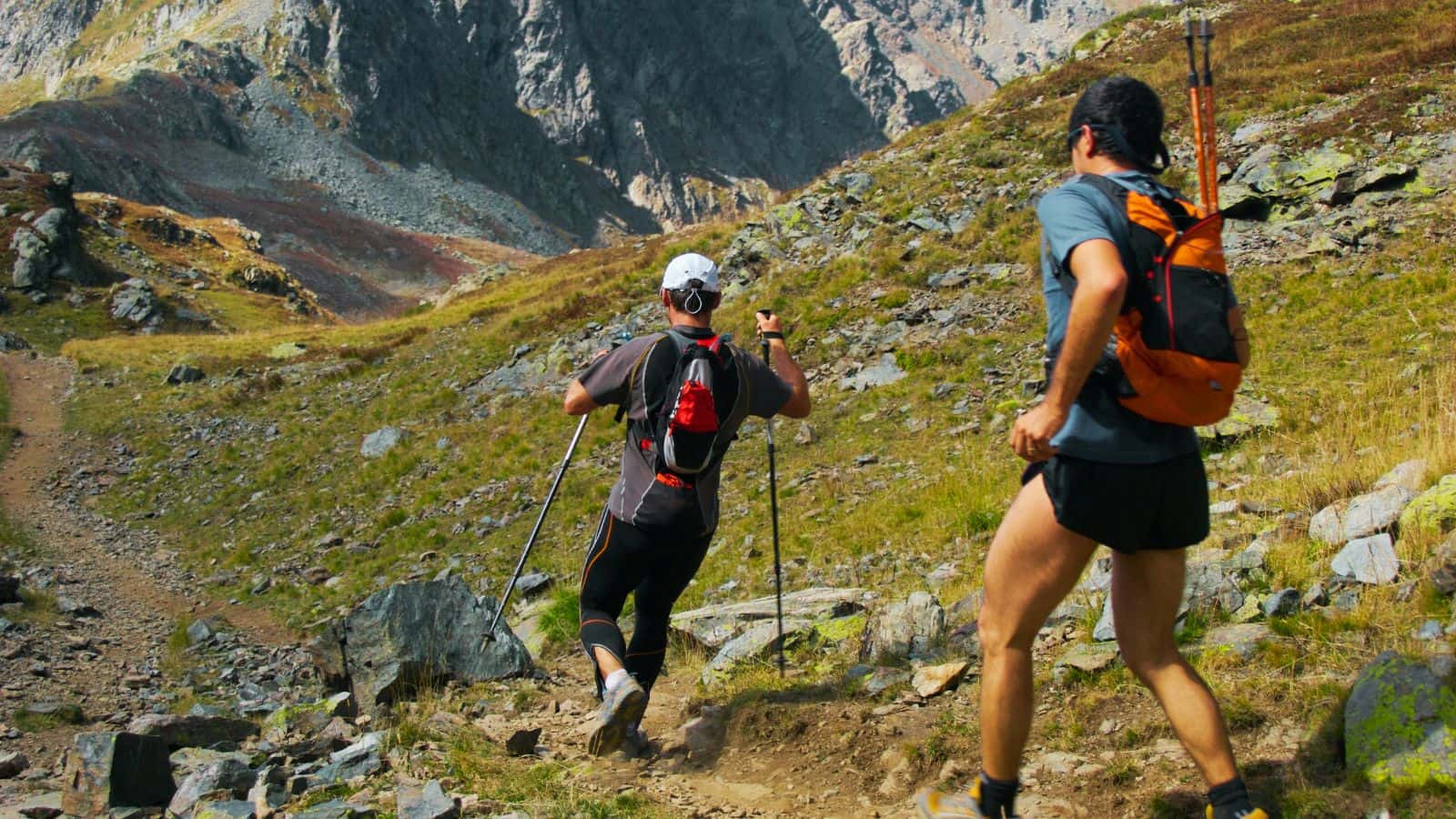 Two hikers with backpacks descending a steep, rocky mountain path, illustrating terrain that frequently triggers knee pain when hiking downhill.