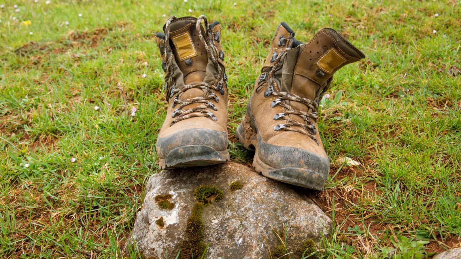 Pair of muddy hiking boots resting on a rock after a hike through deep mud, illustrating post-hike boot care, cleaning and maintenance after wet, boggy trail conditions.