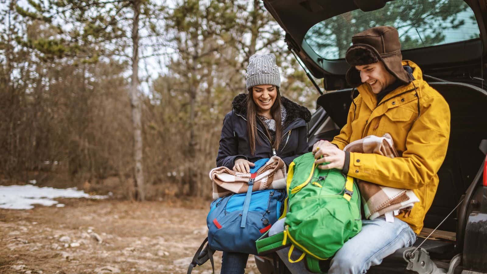 Two hikers in warm jackets resting at the open trunk of a car and packing away backpacks, highlighting post-trek recovery to ease knee pain when hiking downhill.